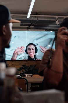 Smiling woman on a video call, viewed from a modern office setting with two people.