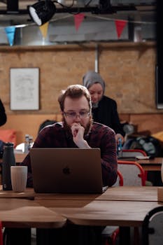 Young adults working on laptops in a cozy London cafe, collaborating and focused.