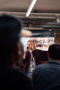 Woman speaks at a seminar in London with an engaged audience. Indoor setting.