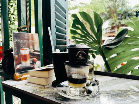 Refreshing Vietnamese coffee in a glass with a phin filter, set on a café table surrounded by tropical plants.
