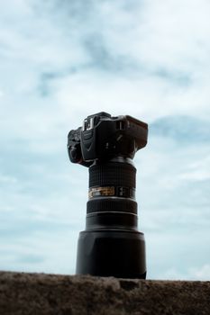 Creative shot of a DSLR camera with telephoto lens against a cloudy sky.