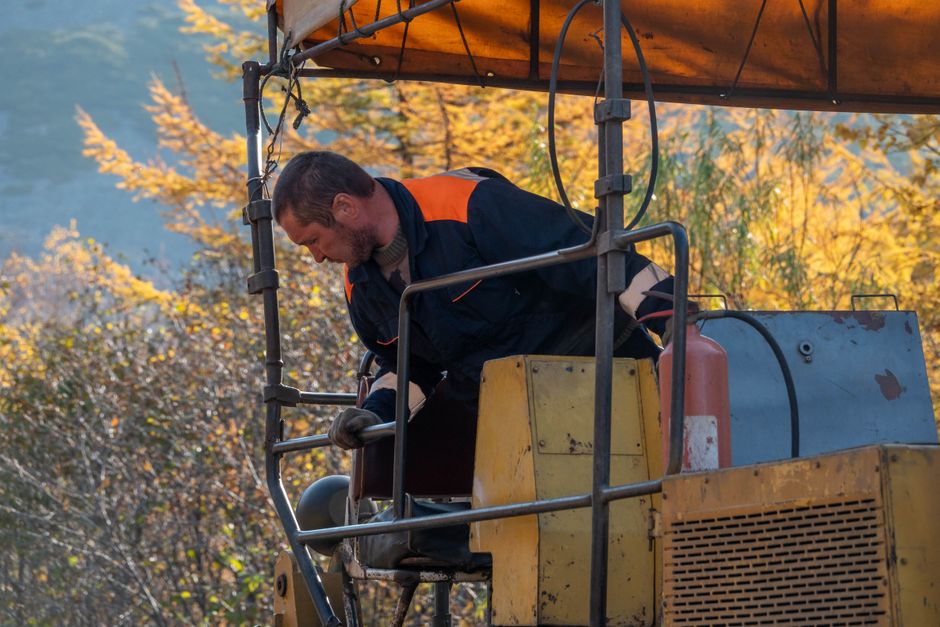 A construction worker in a blue uniform operating heavy machinery outdoors during autumn. A construction worker in a blue uniform operating heavy machinery outdoors during autumn.