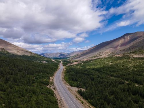 Free Vast aerial view of a winding highway cutting through lush green mountains under a blue sky. Stock Photo