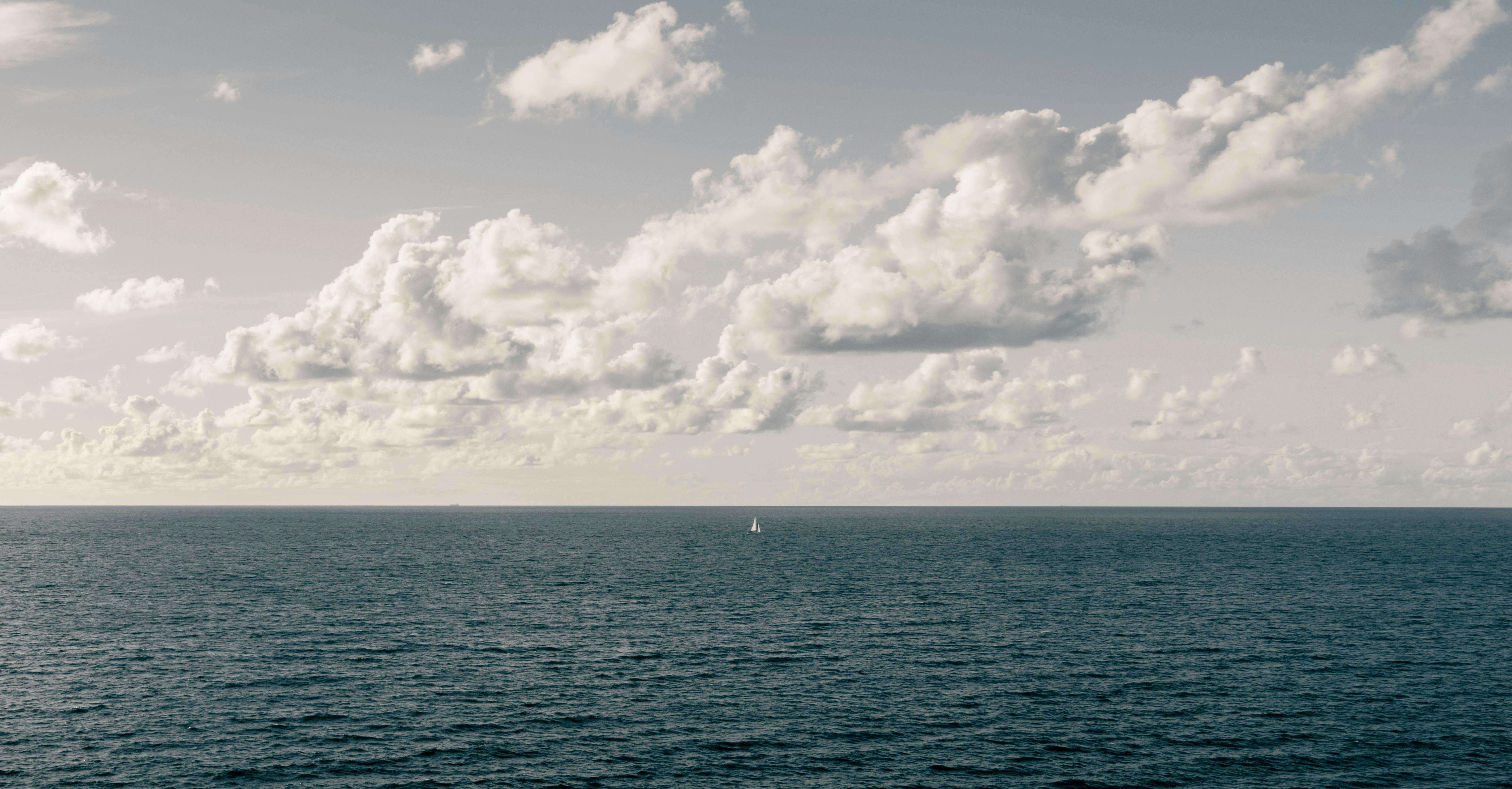 Calm seascape featuring a lone yacht under a cloudy skyline, perfect for a tranquil background.