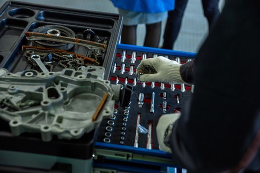 A mechanic in gloves organizing engine parts and tools in a workshop setting.
