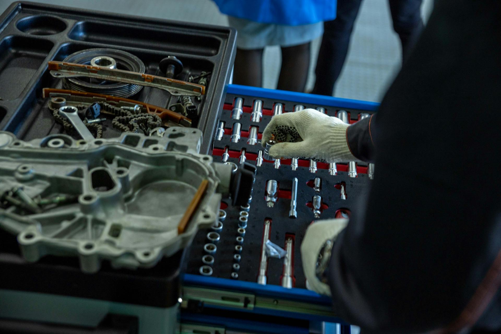 A mechanic in gloves organizing engine parts and tools in a workshop setting.