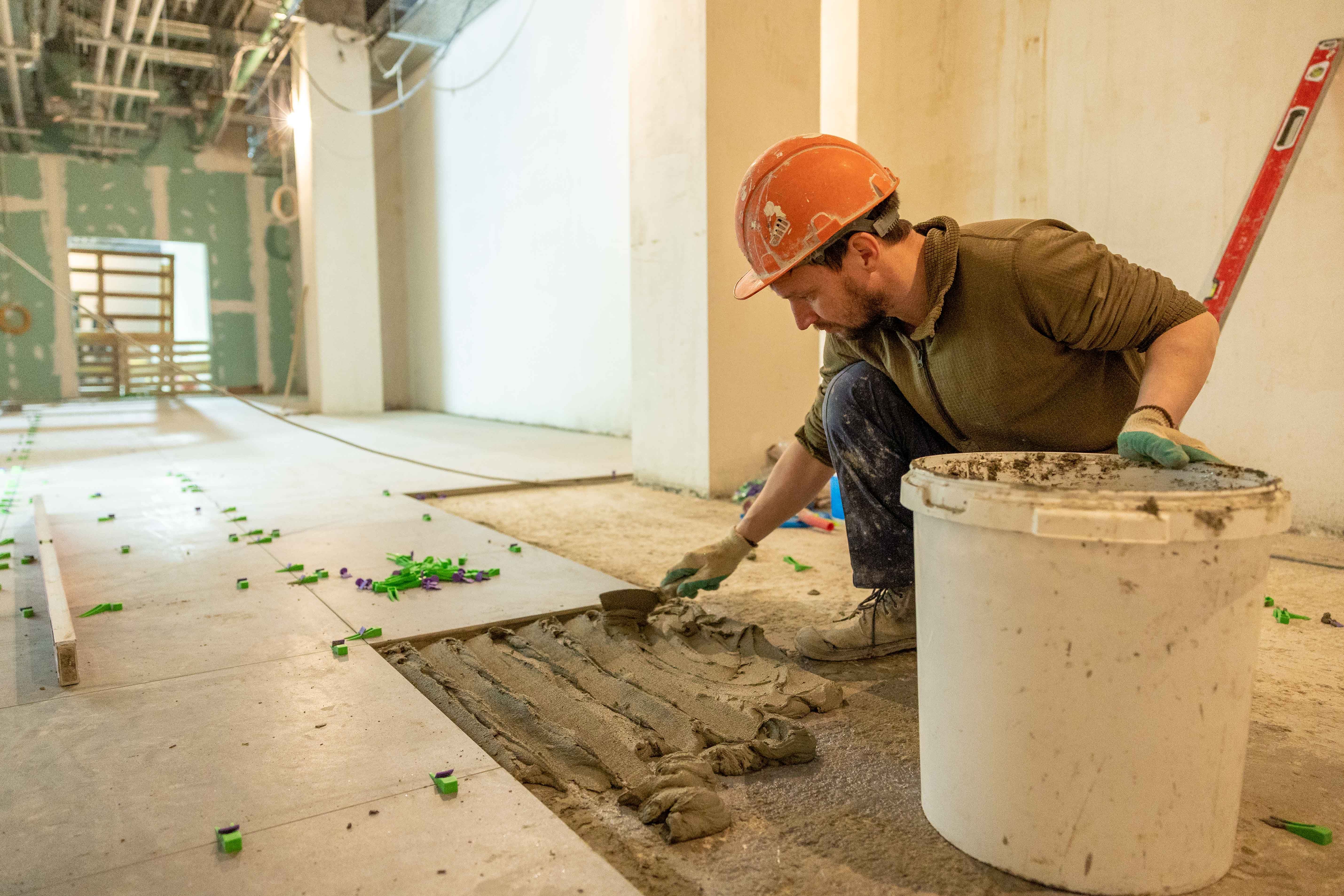 Restricted Builders Licence QLD: Classes, Scope, Eligibility & Application 7 Construction worker laying tiles during an indoor renovation project