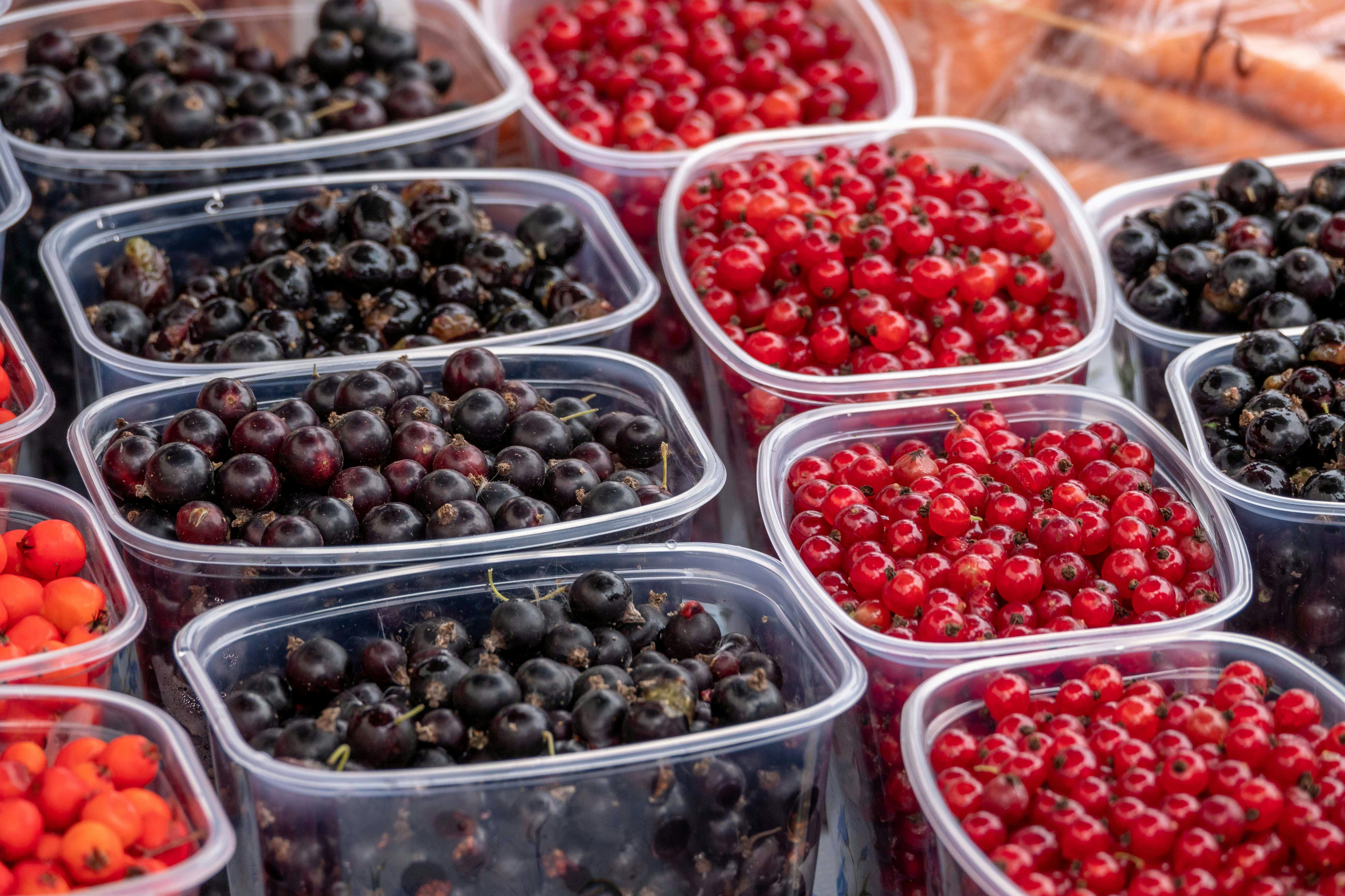 Close-up view of ripe blackcurrants and redcurrants in plastic containers on display at a market.