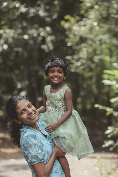 Free Happy mother holding her daughter in a forest setting, both smiling warmly at the camera. Stock Photo