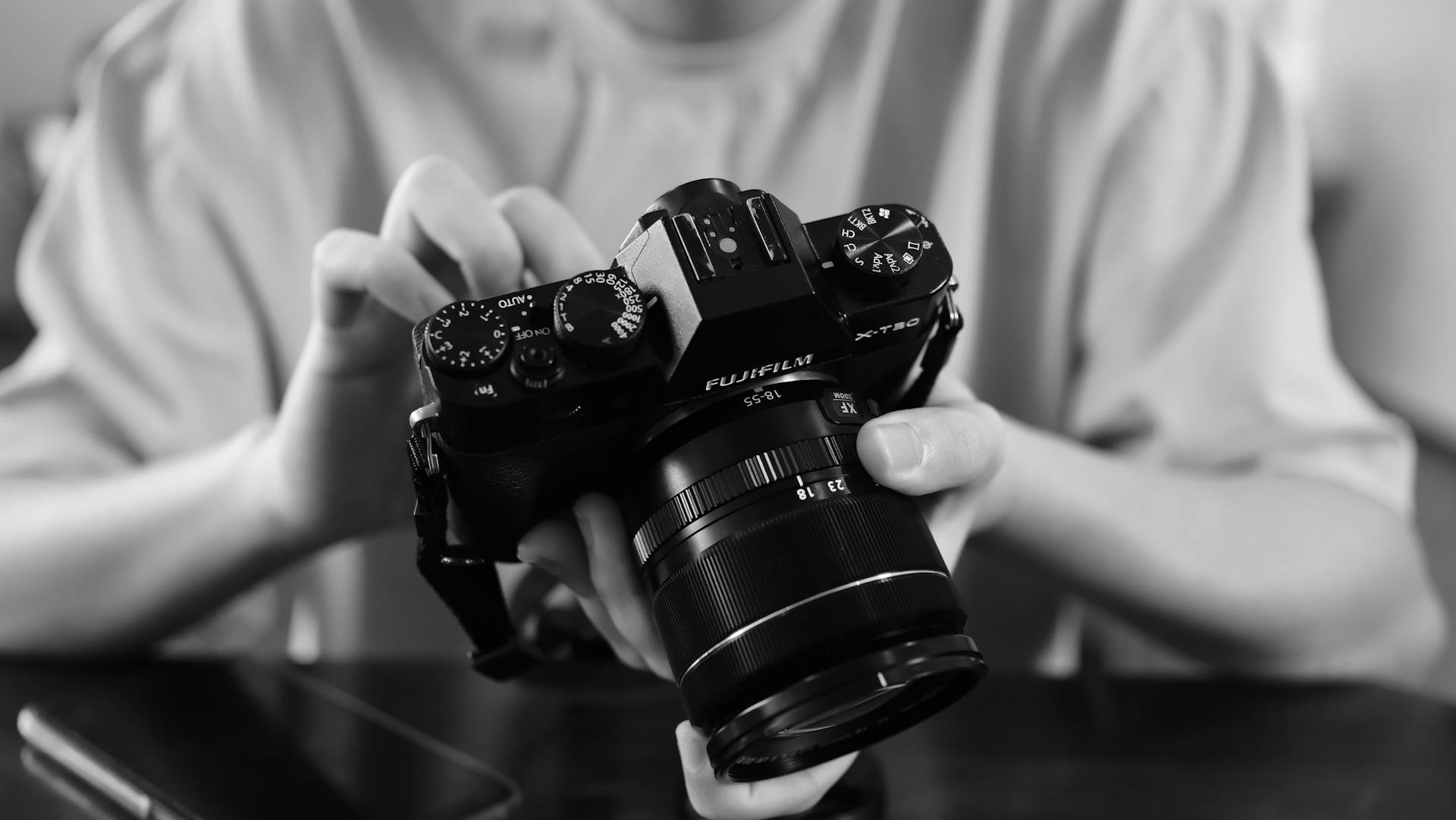 Close-up black and white shot of someone adjusting settings on a Fujifilm X-T20 camera.