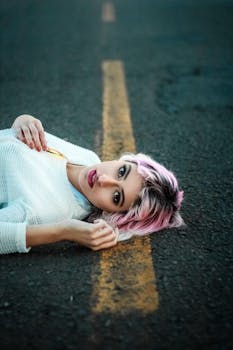 一位粉红色头发的年轻女子躺在城市道路上，向上凝视的肖像