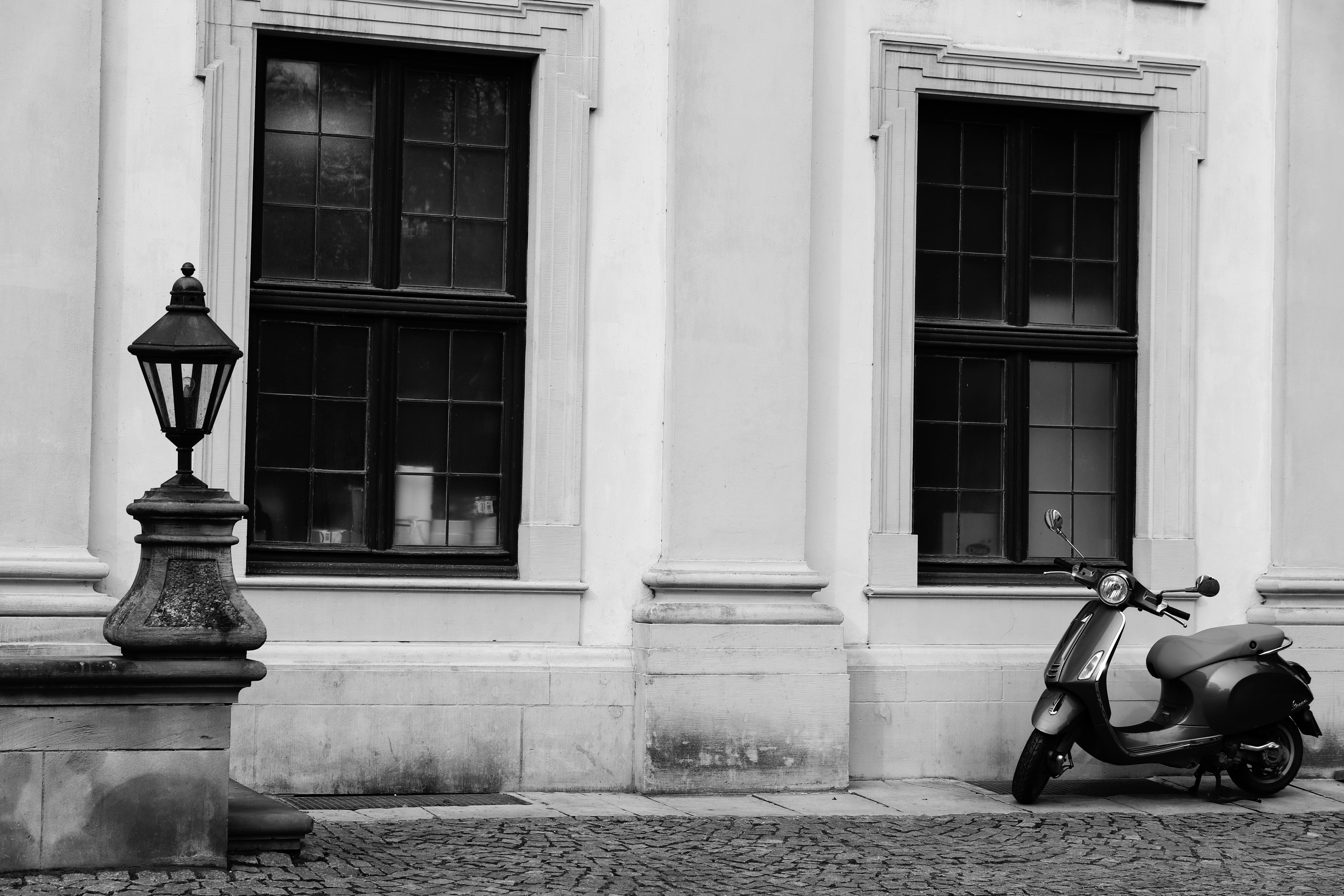 Black and white photo of a vintage building facade with a scooter and lantern.