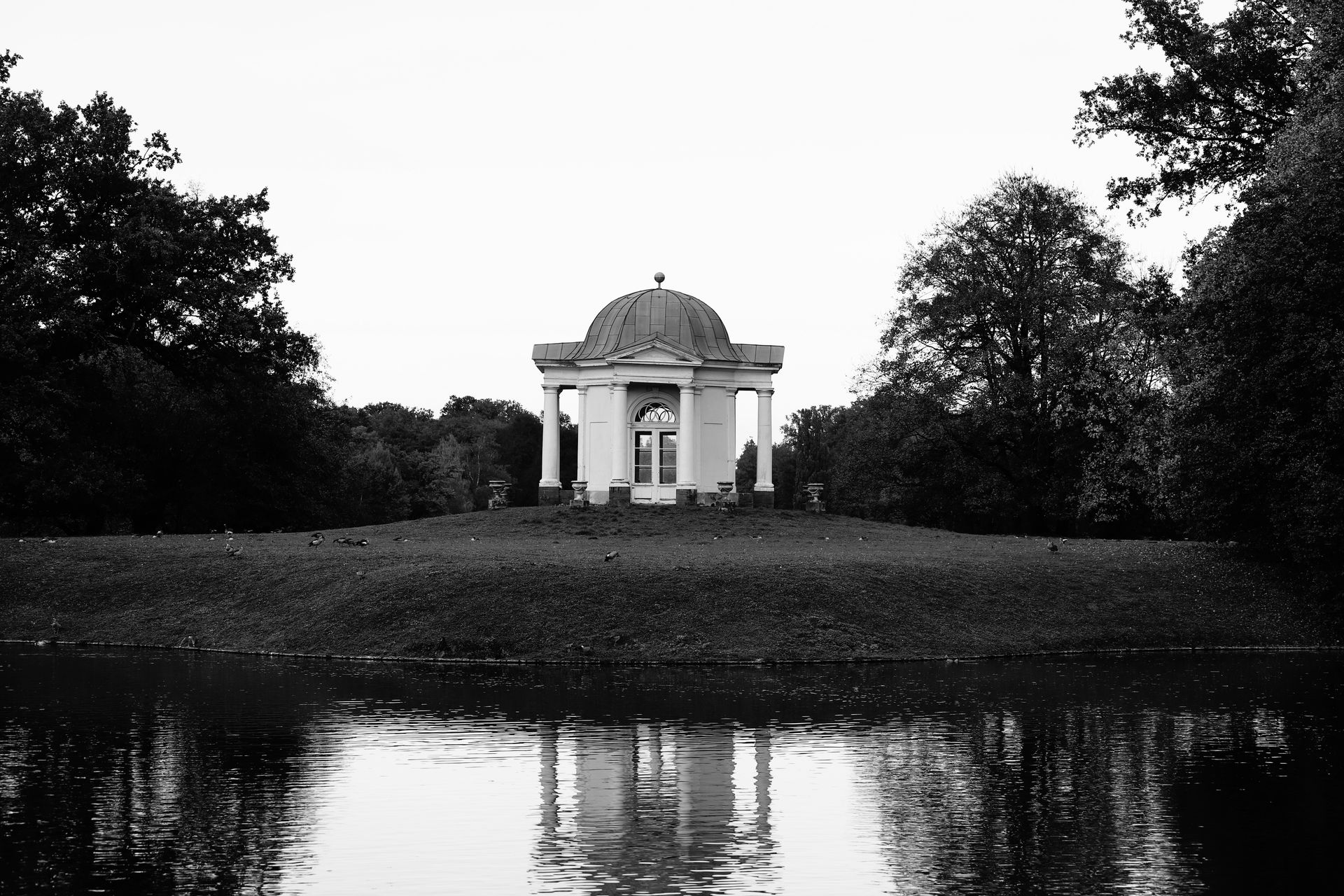Monochrome image of a gazebo by a lake surrounded by trees in Kassel, Germany.