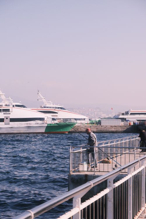 Free Serene moment of fishing by the docks with large boats in view, capturing tranquility. Stock Photo