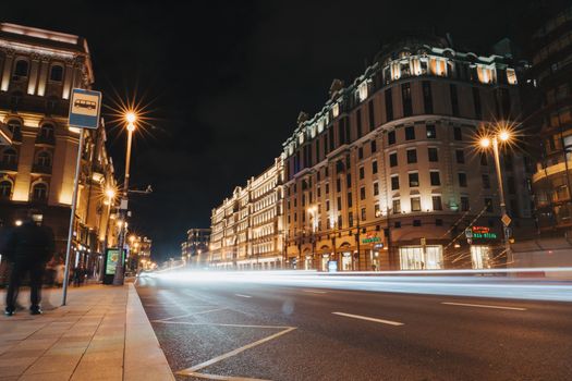 Dynamic city street at night with light trails and illuminated buildings.