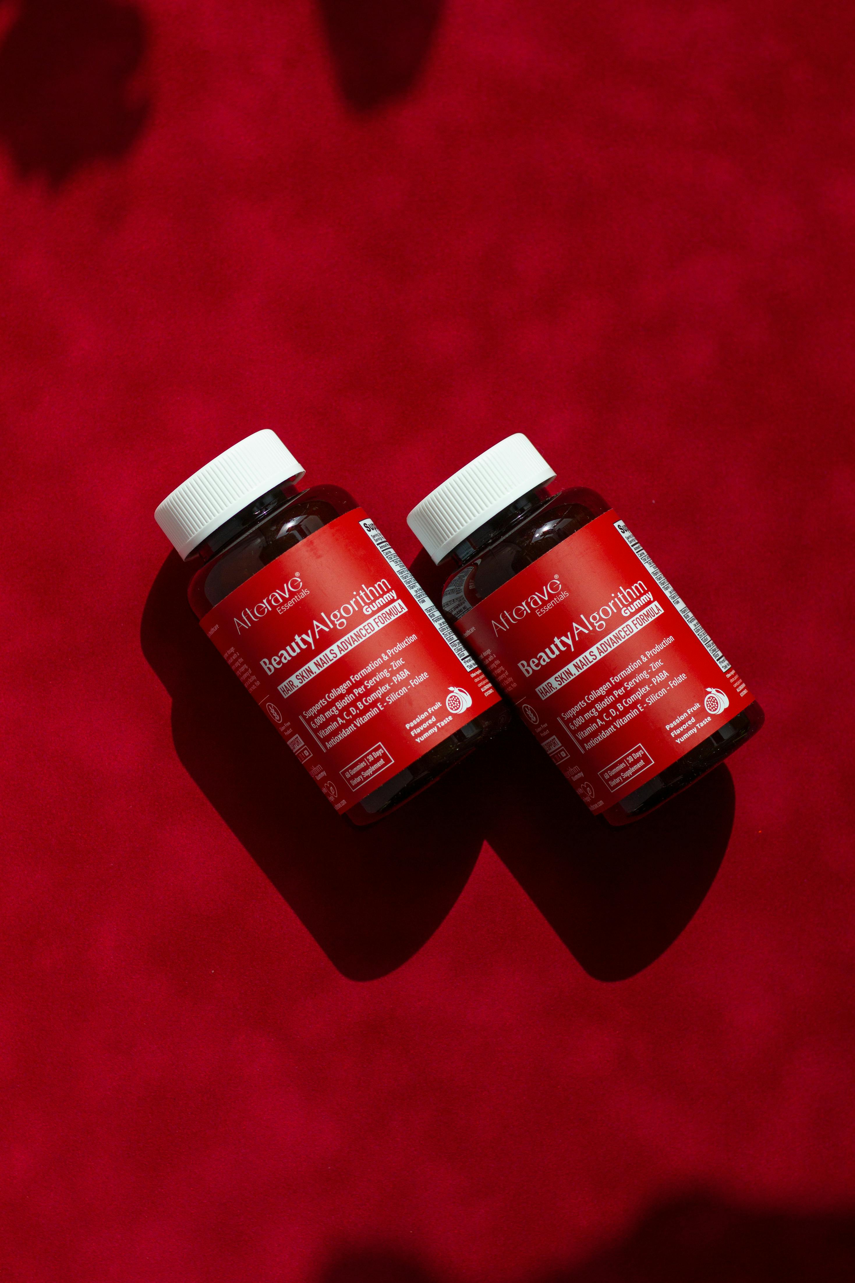 Two beauty supplement bottles lie on a vivid red background, creating a vibrant visual impact.