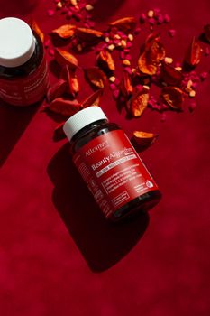 Vitamins on red background with scattered rose petals, promoting beauty care.