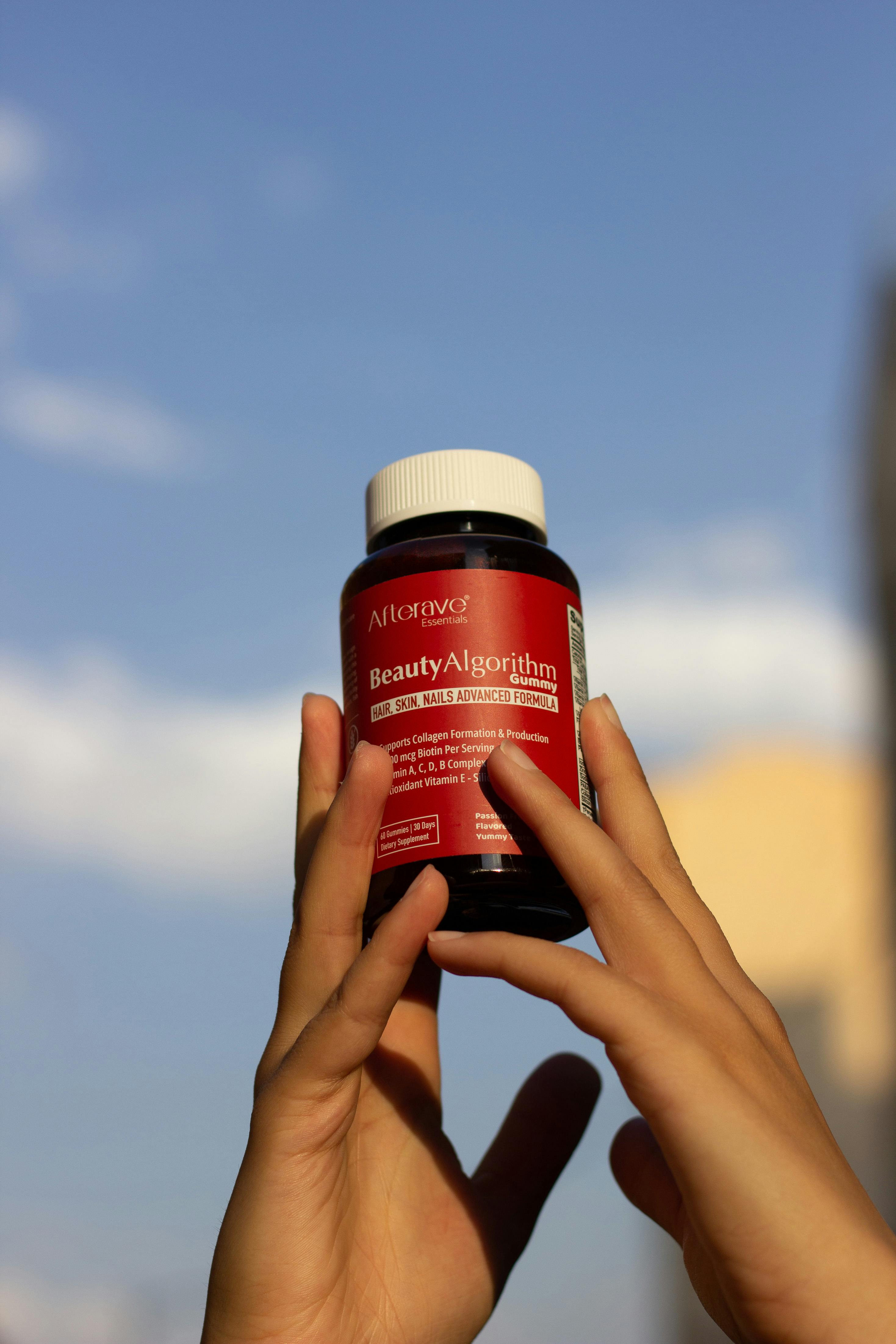 Hands holding Afterave BeautyAlgorithm vitamin supplement against a clear blue sky in Los Angeles, perfect for health concepts.