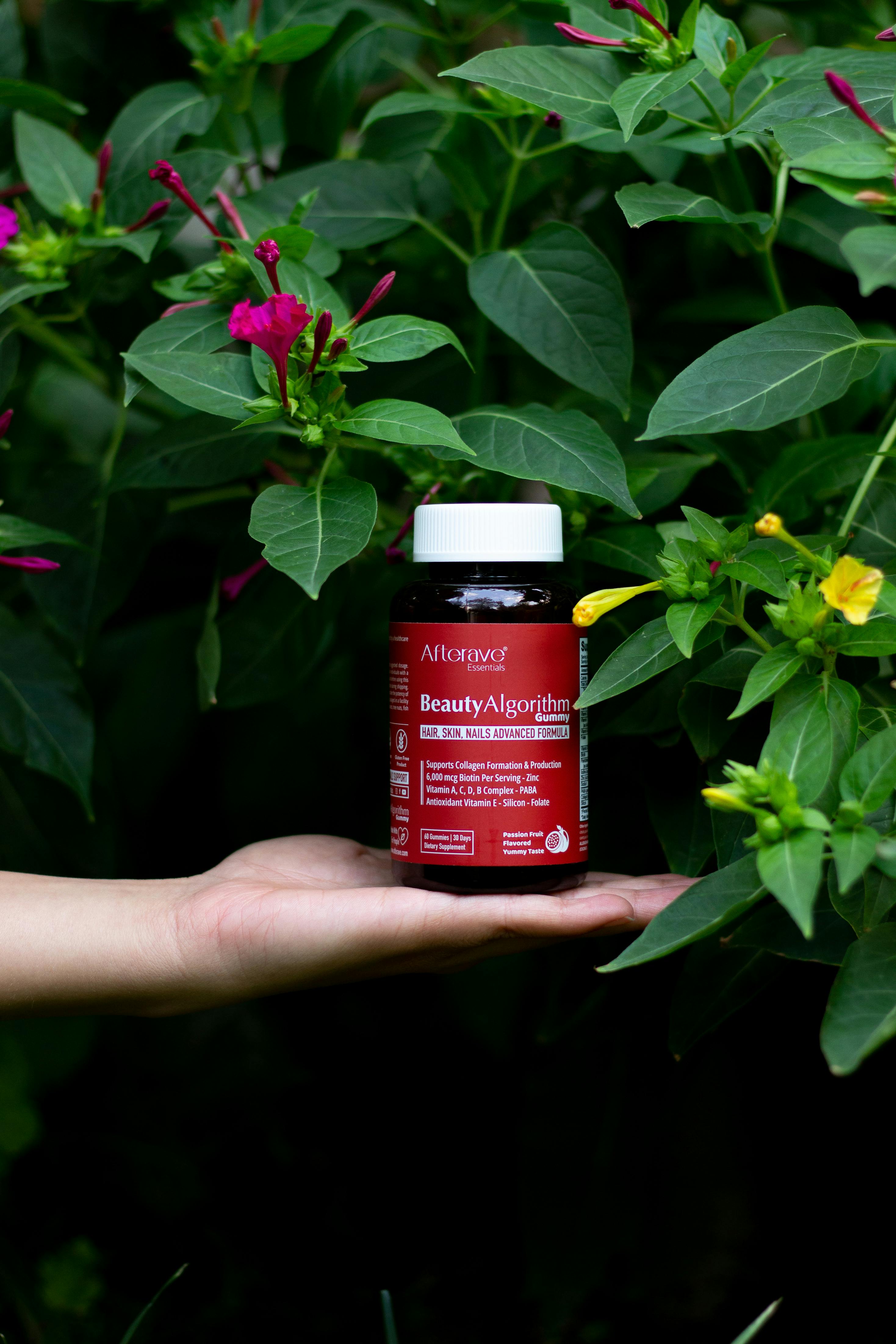 Beauty supplement displayed on a hand surrounded by lush green foliage and colorful flowers.
