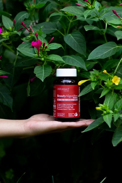 Free Beauty supplement displayed on a hand surrounded by lush green foliage and colorful flowers. Stock Photo