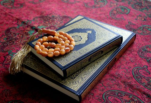 Free An arrangement of the Holy Quran with a Tasbih rosary on a traditional red patterned fabric. Stock Photo