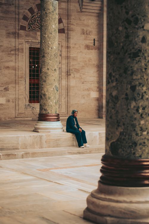 Free A solitary woman sits between ornate columns in a historic stone courtyard. Stock Photo