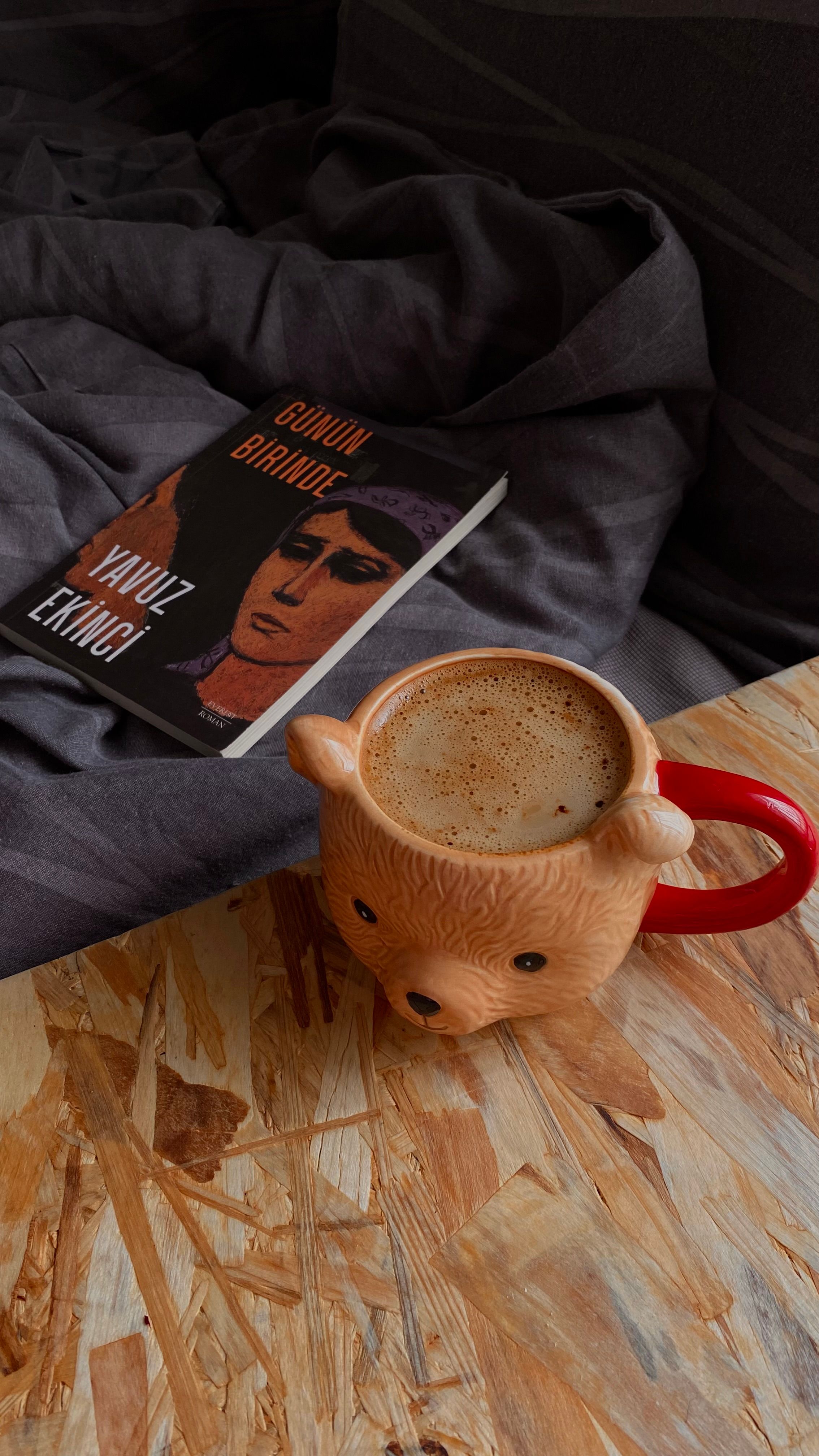 Warm and inviting setup with a bear mug of coffee and a book on a cozy bed.