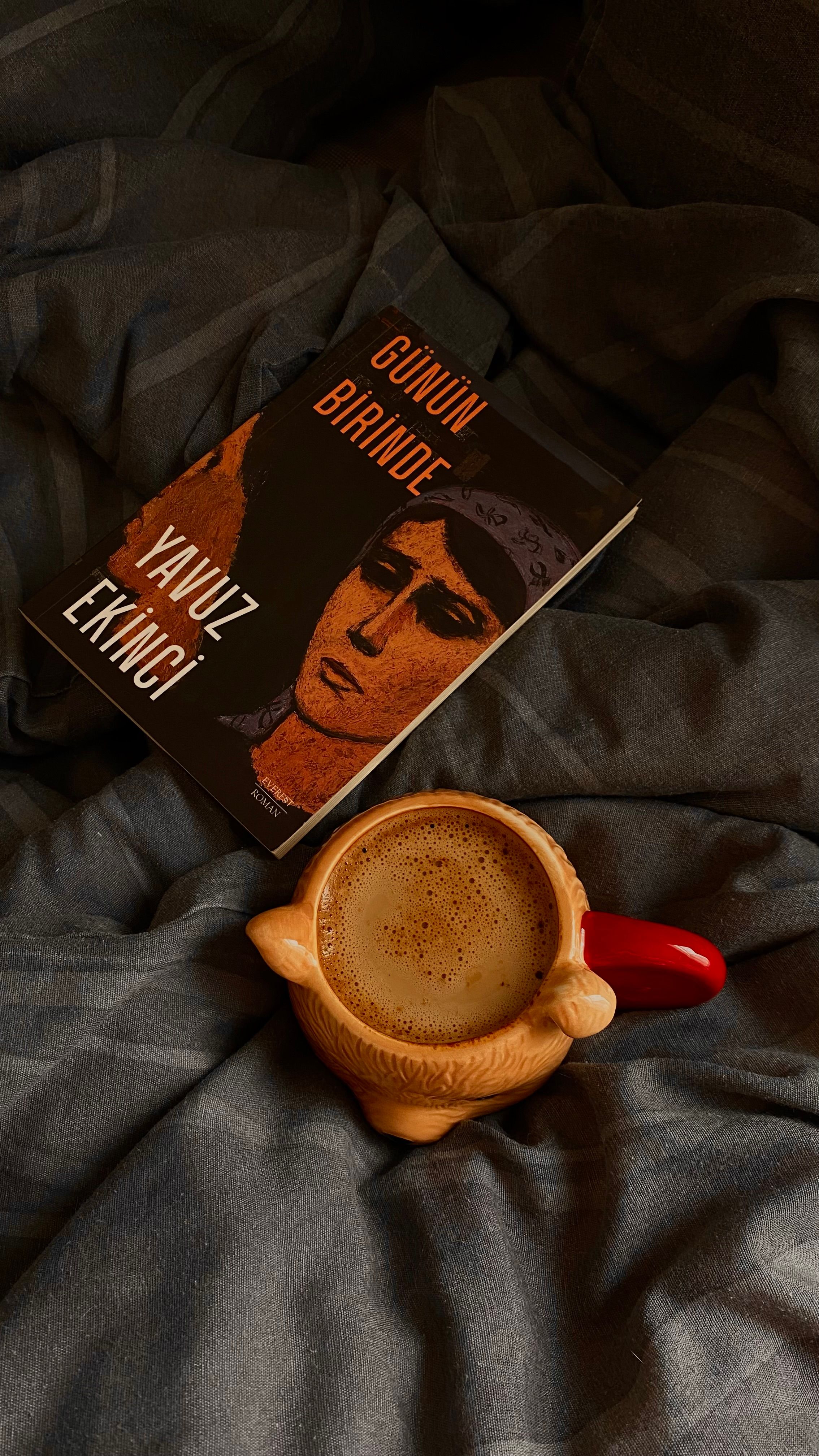Warm and cozy scene with coffee and book on a bed with a grey blanket.