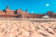 在西班牙塞维利亚的西班牙广场，蔚蓝的天空下矗立着标志性的喷泉和独特的建筑