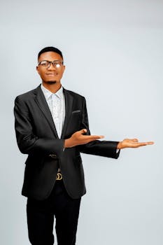 Smiling young man in formal wear presenting something with an open hand gesture.