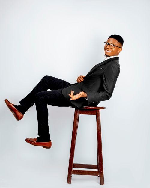 Free Smiling young man in black suit sits confidently on a stool indoors. Stock Photo