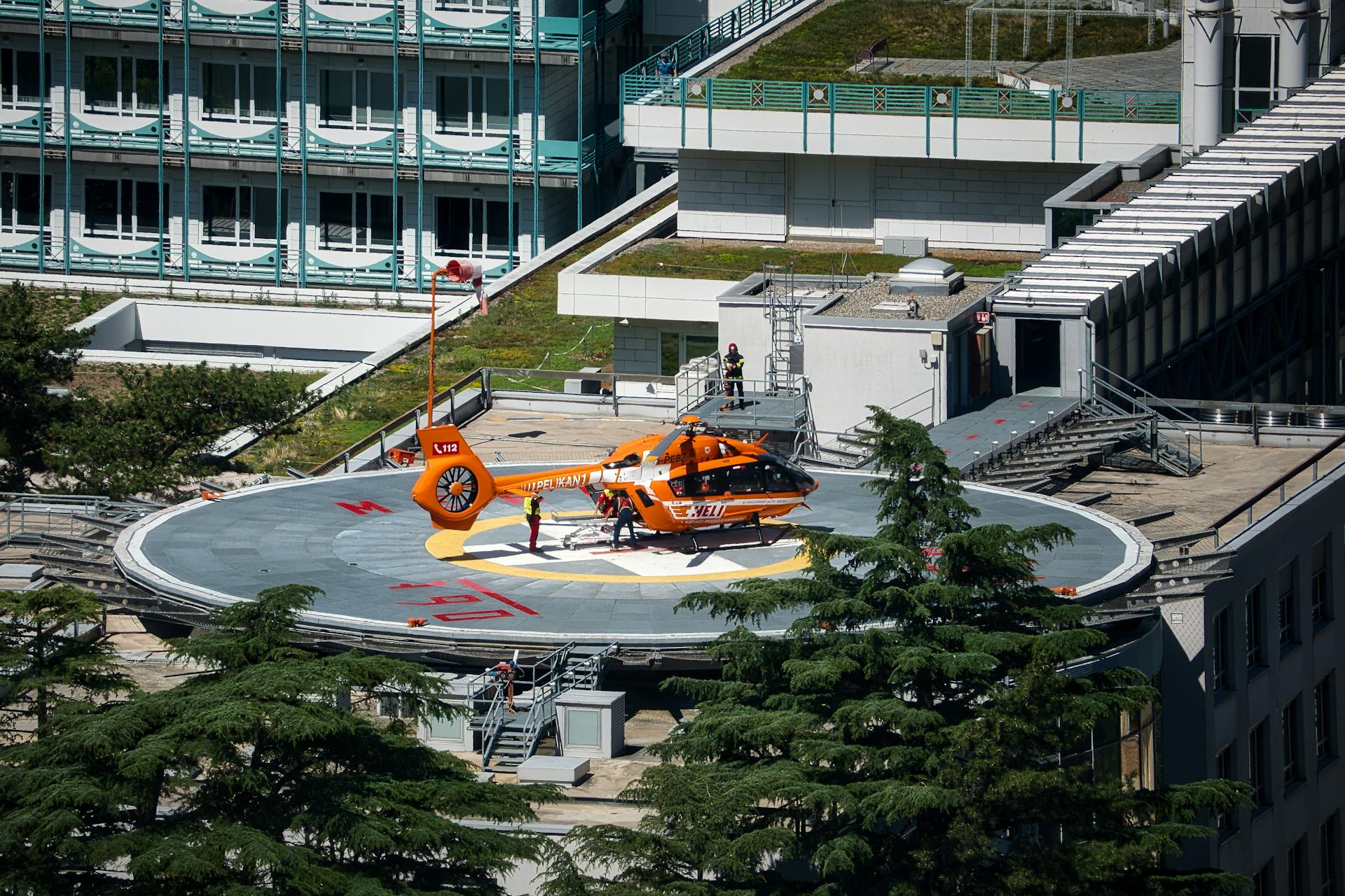 Orange helicopter on helipad of hospital building in Merano, Italy, during daytime.