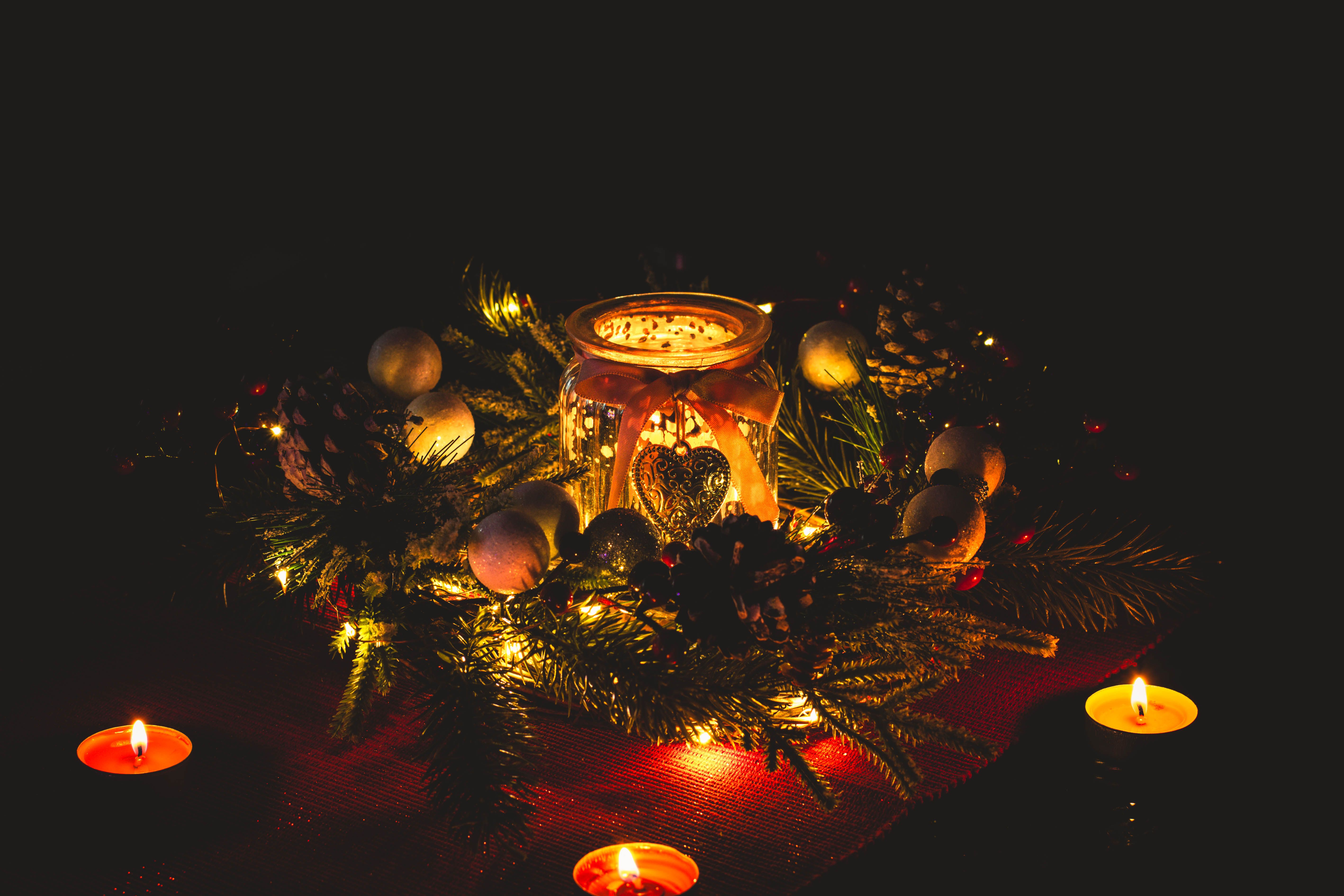 Warm and festive candle arrangement with pine branches and ornaments, perfect for holiday decor.