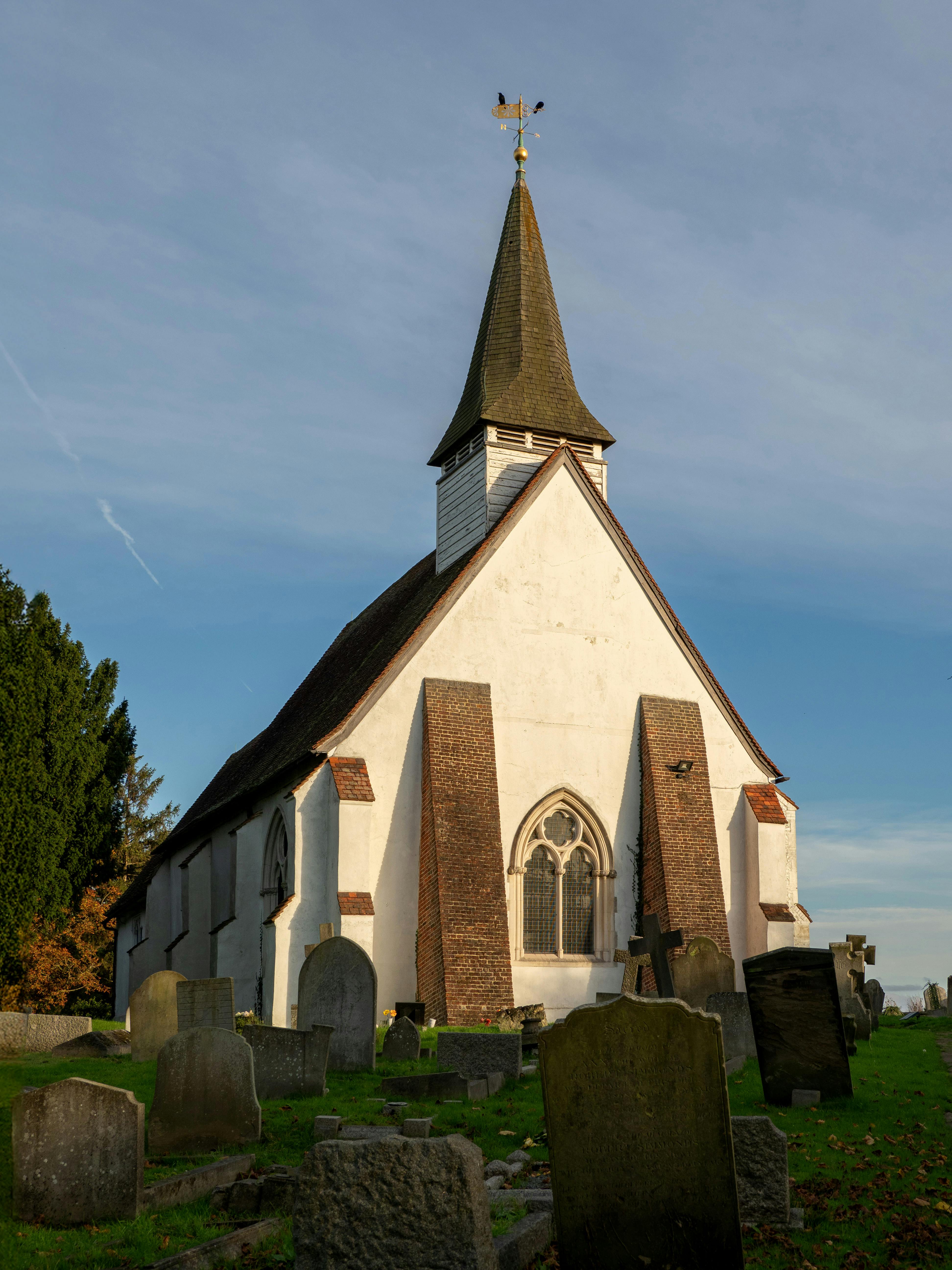 Old Anglican church surrounded by tombstones under a clear sky.