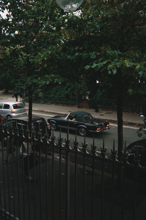 Free Classic black convertible car cruising down a tree-lined urban street. Stock Photo