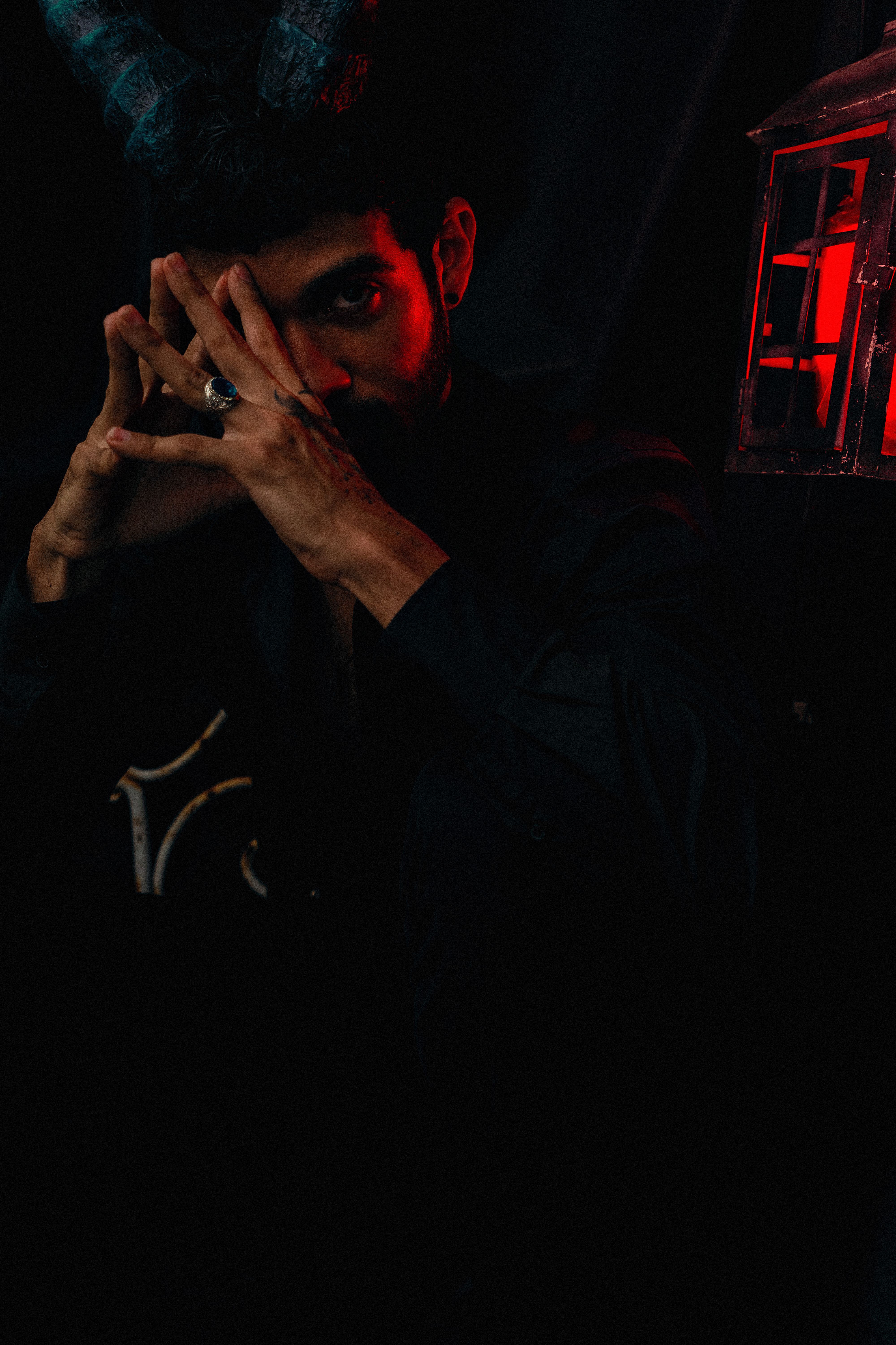 Dark artistic portrait featuring a man with horns and red lighting for a mysterious effect.