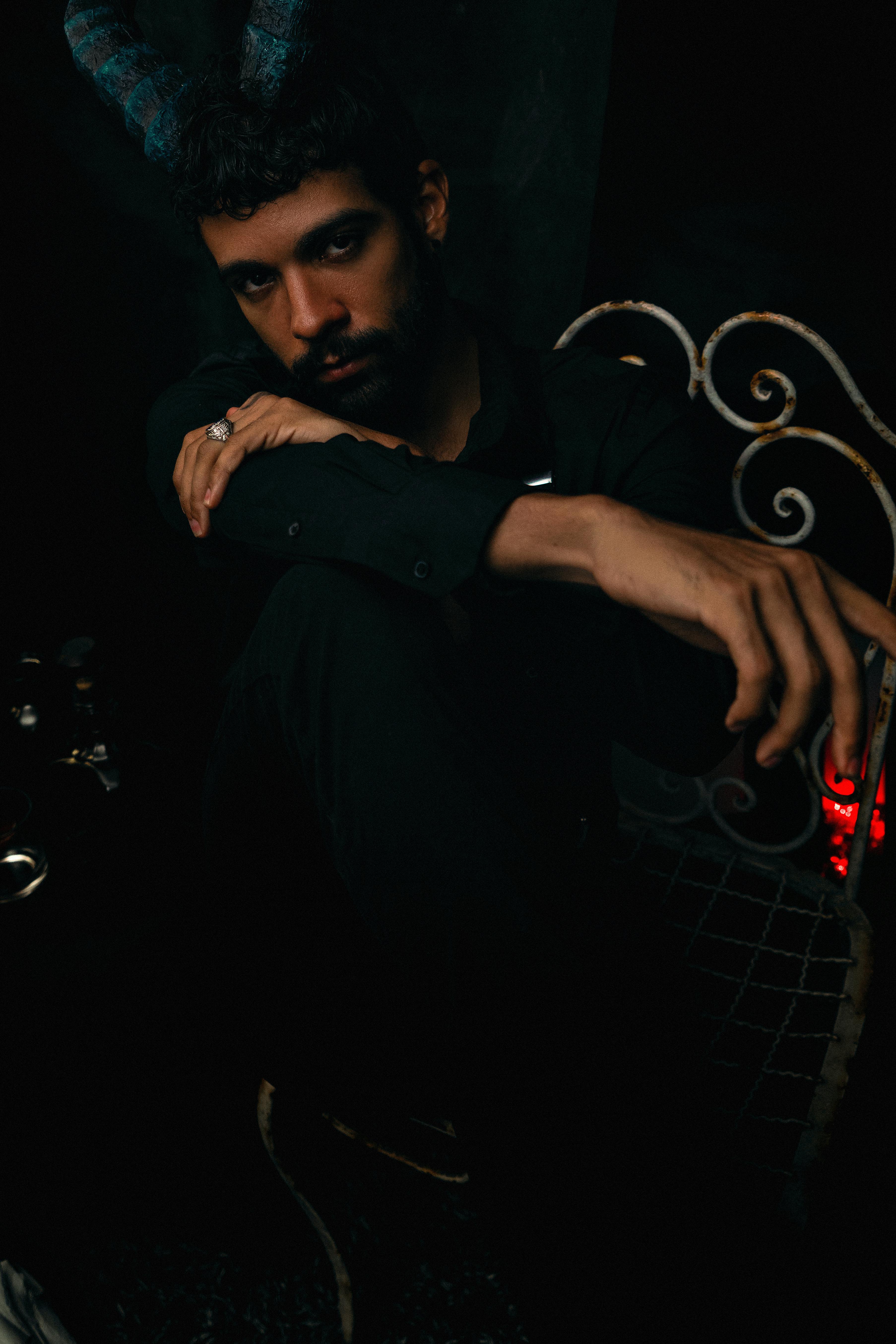 Gratuit Portrait dramatique d'un homme aux cornes sombres, assis dans une lumière tamisée. Photos