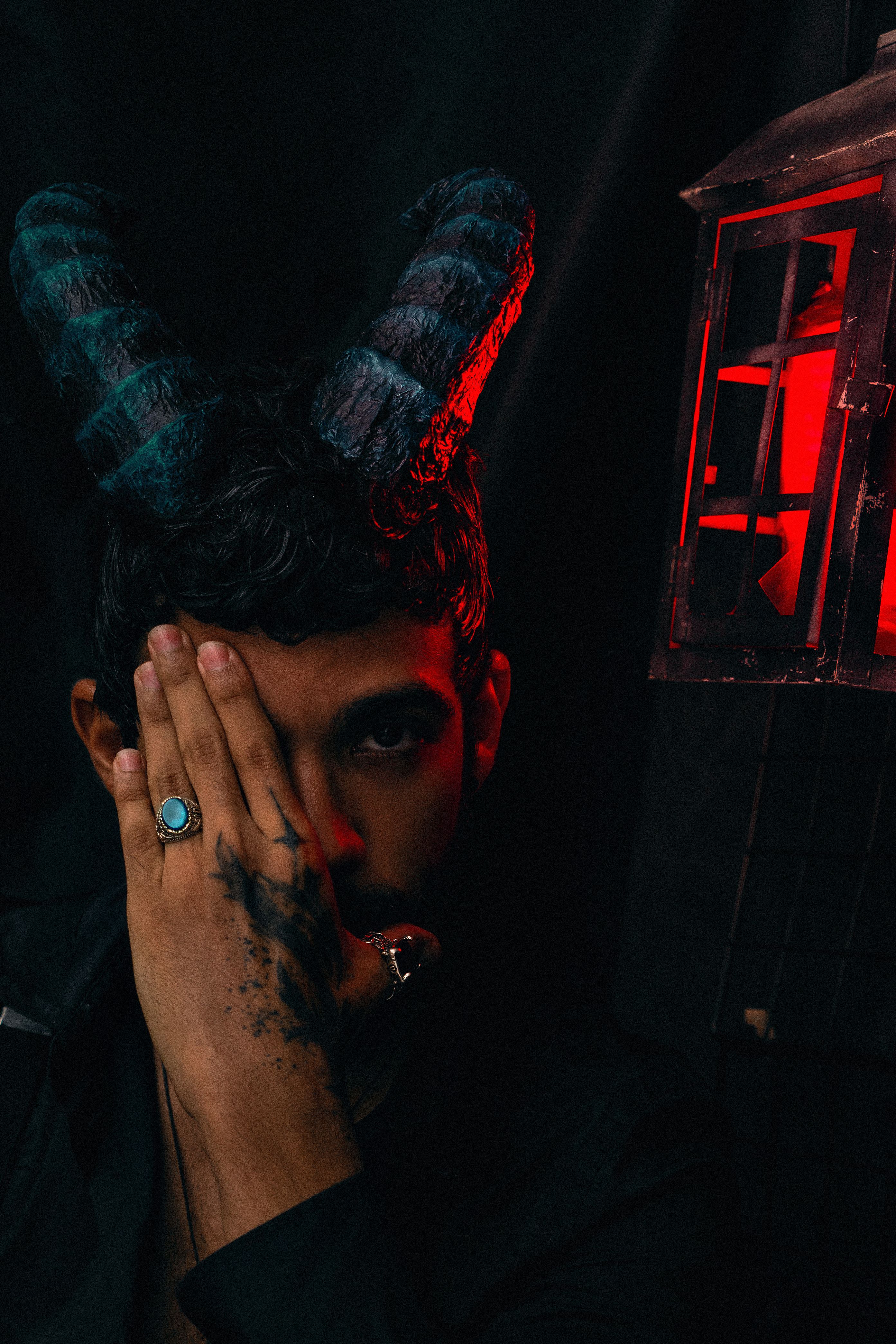 A mysterious portrait featuring a person with blue horns and a red lantern casting an eerie glow.