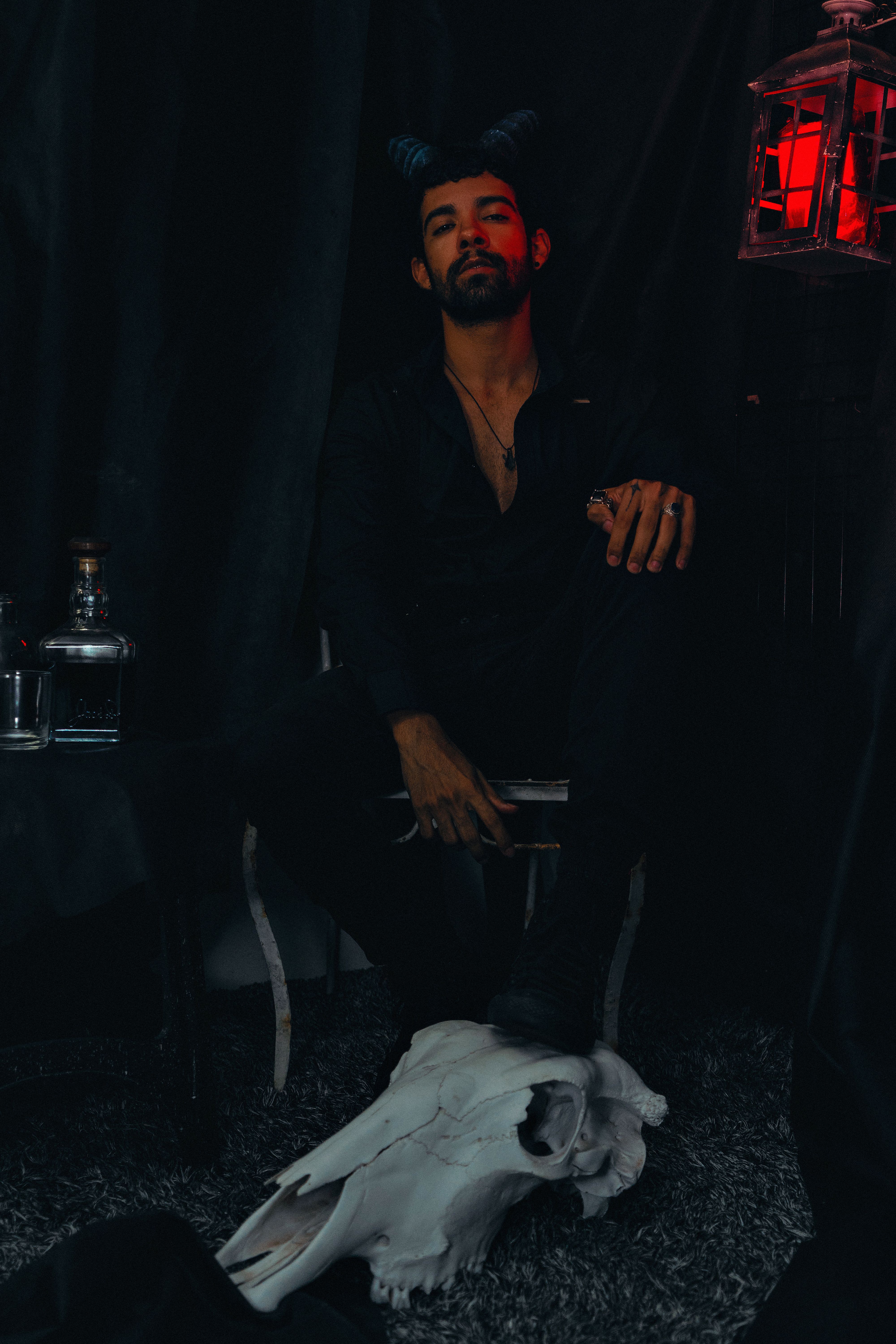 Dark themed portrait of a man with horns sitting by a skull in atmospheric lighting.