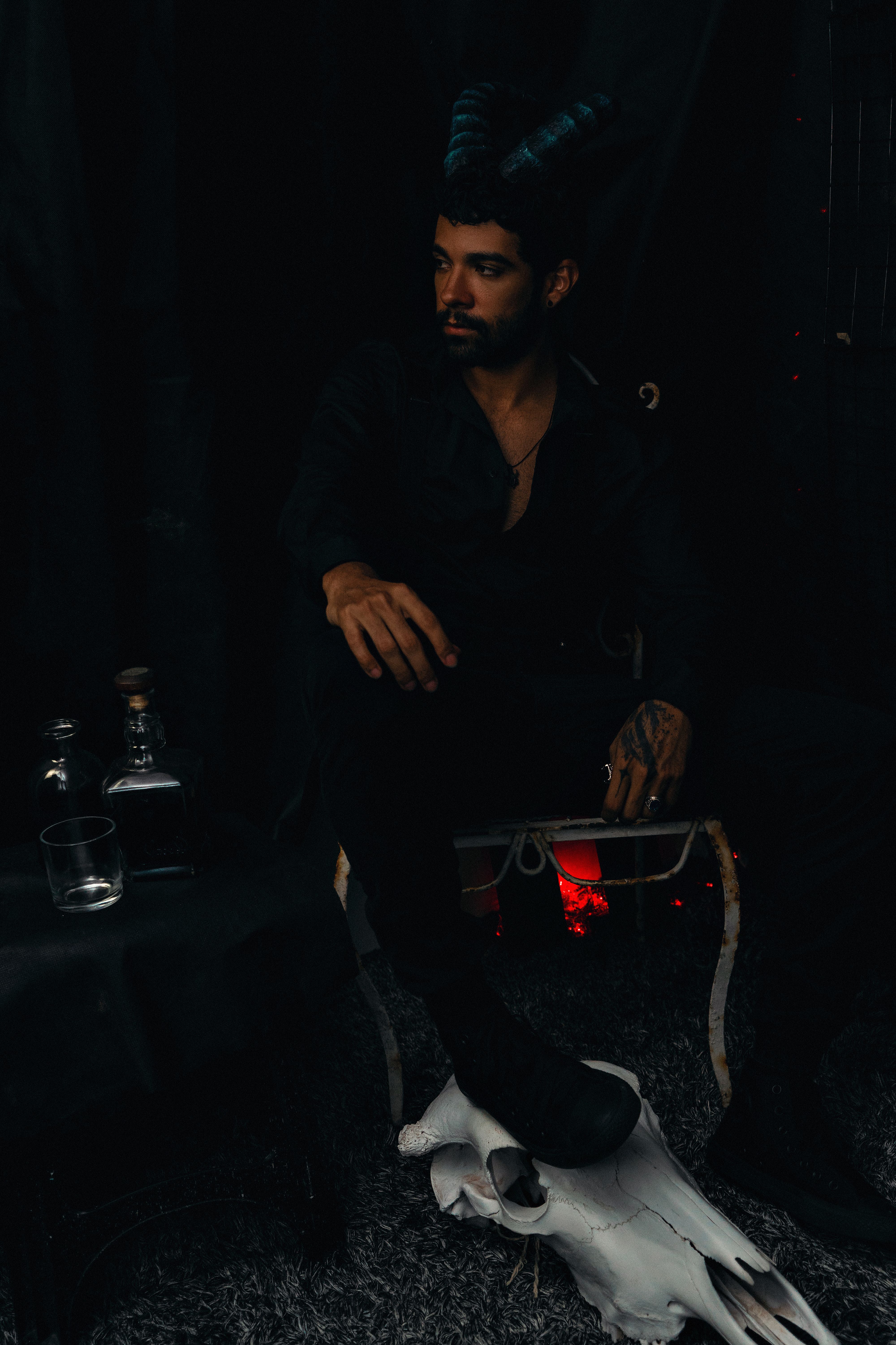 A man with horns sits in a dimly lit room with dark, enigmatic decor.