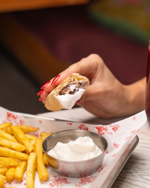 Free Close-up of hand holding tasty wrap with fries and sauce on a tray. Stock Photo