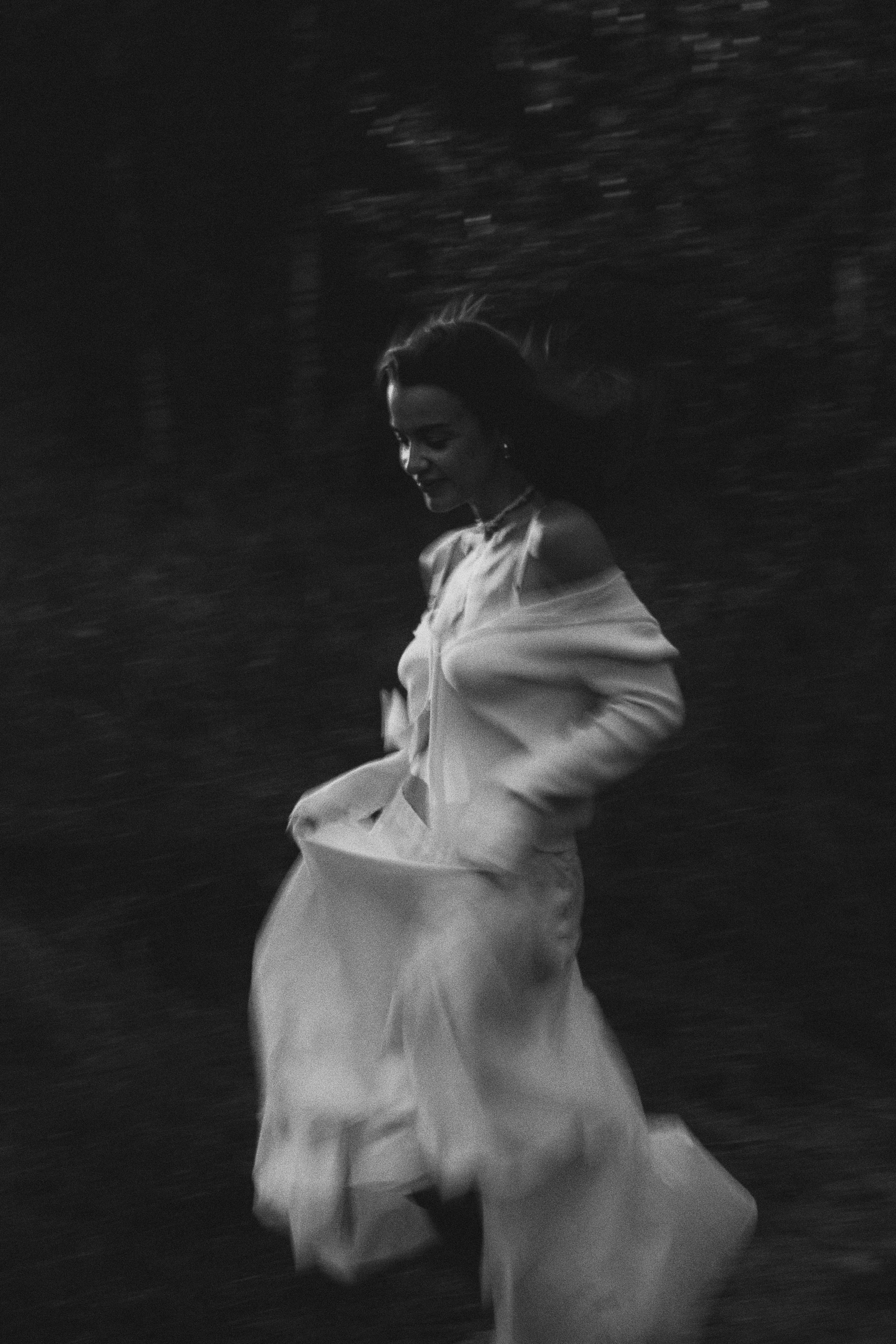 A woman in a flowing dress runs gracefully in a dark, blurry atmosphere capturing movement.