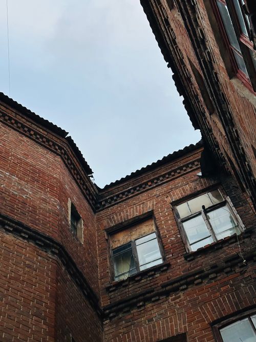 Free Low angle view of an aged brick building with rustic, weathered windows against a clear sky. Stock Photo