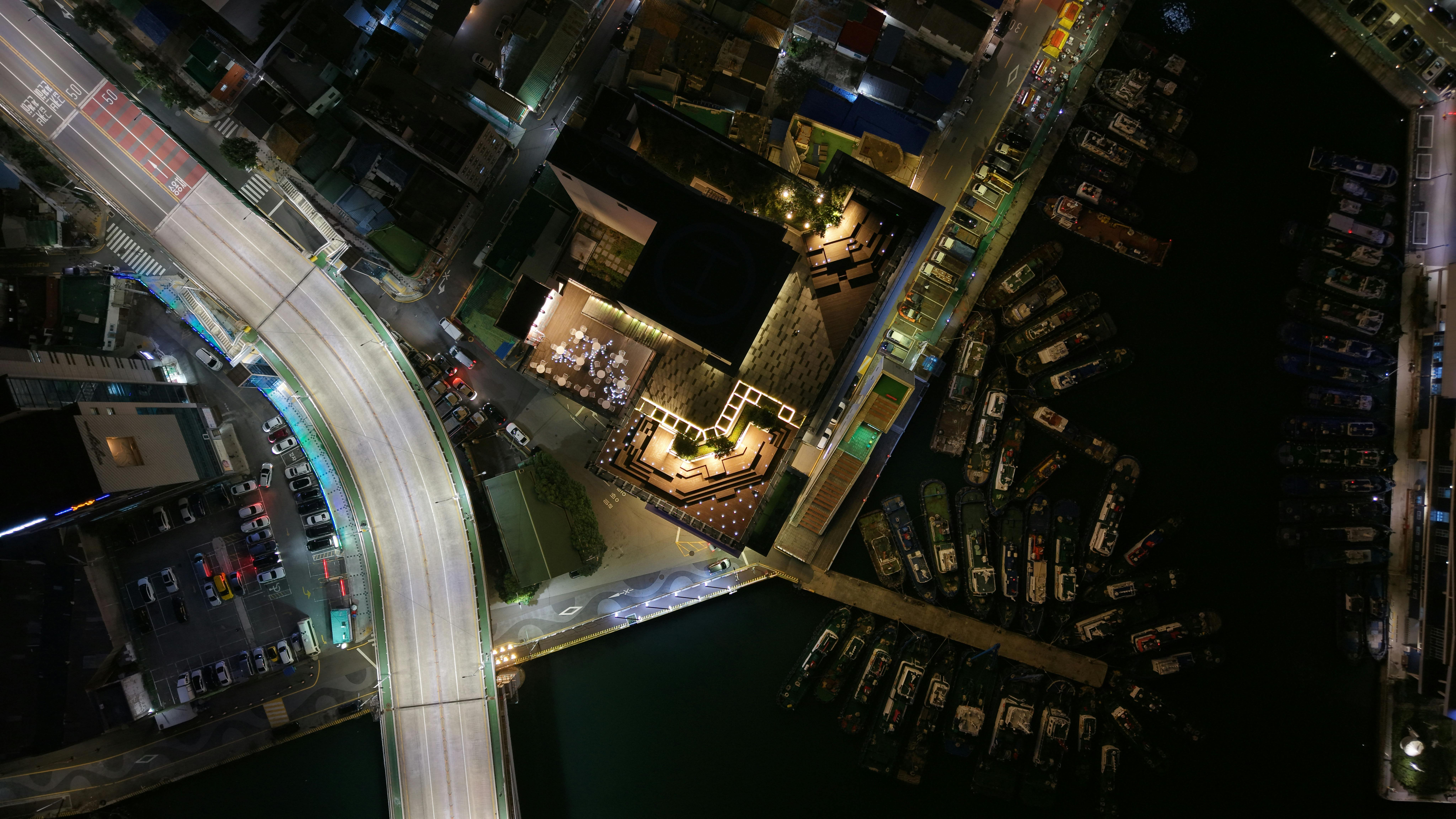 A captivating aerial image of Busan's cityscape at night, featuring illuminated roads and docked boats.