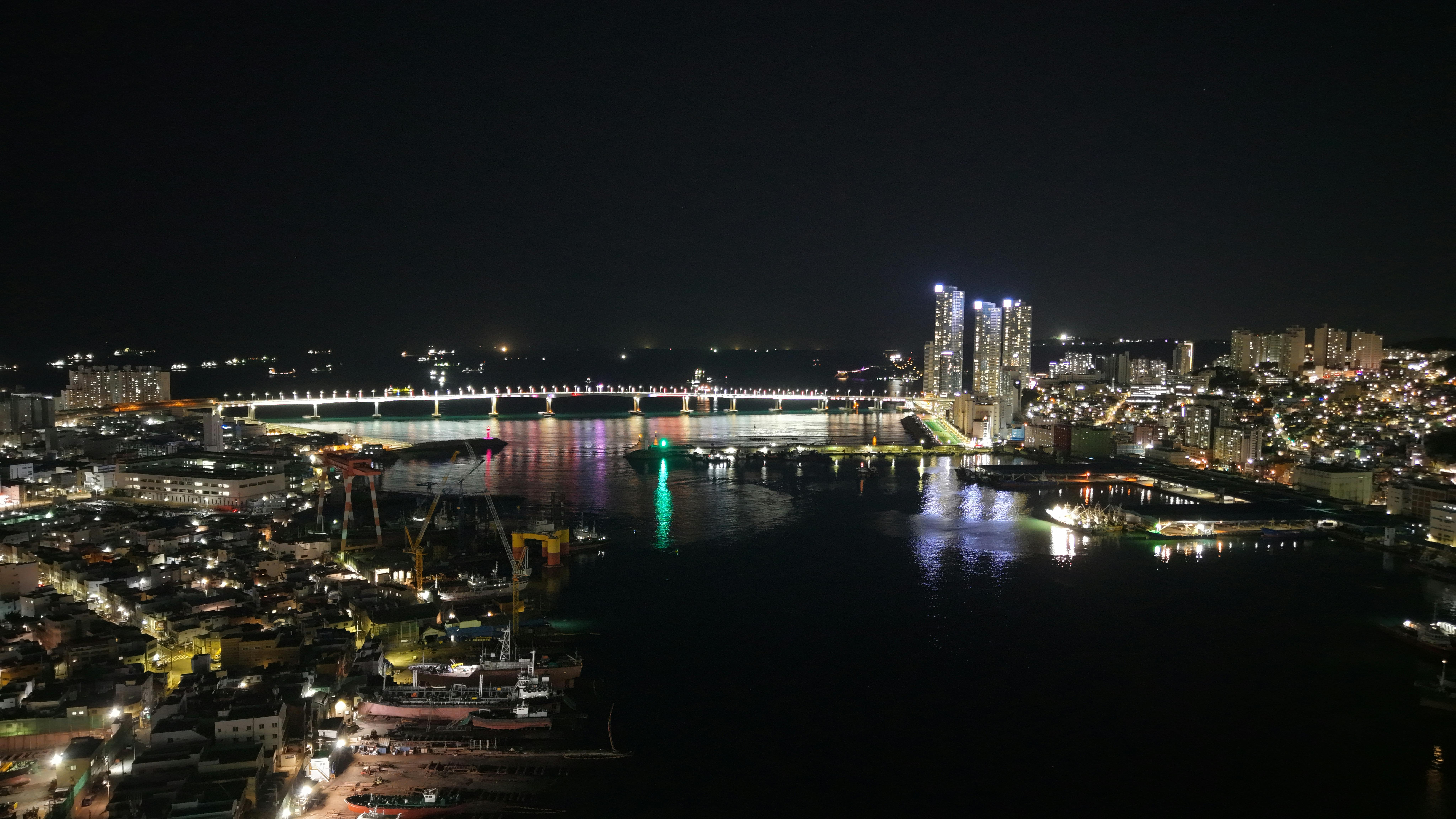 Stunning night view of Busan's illuminated skyline and bridge reflecting on the water.