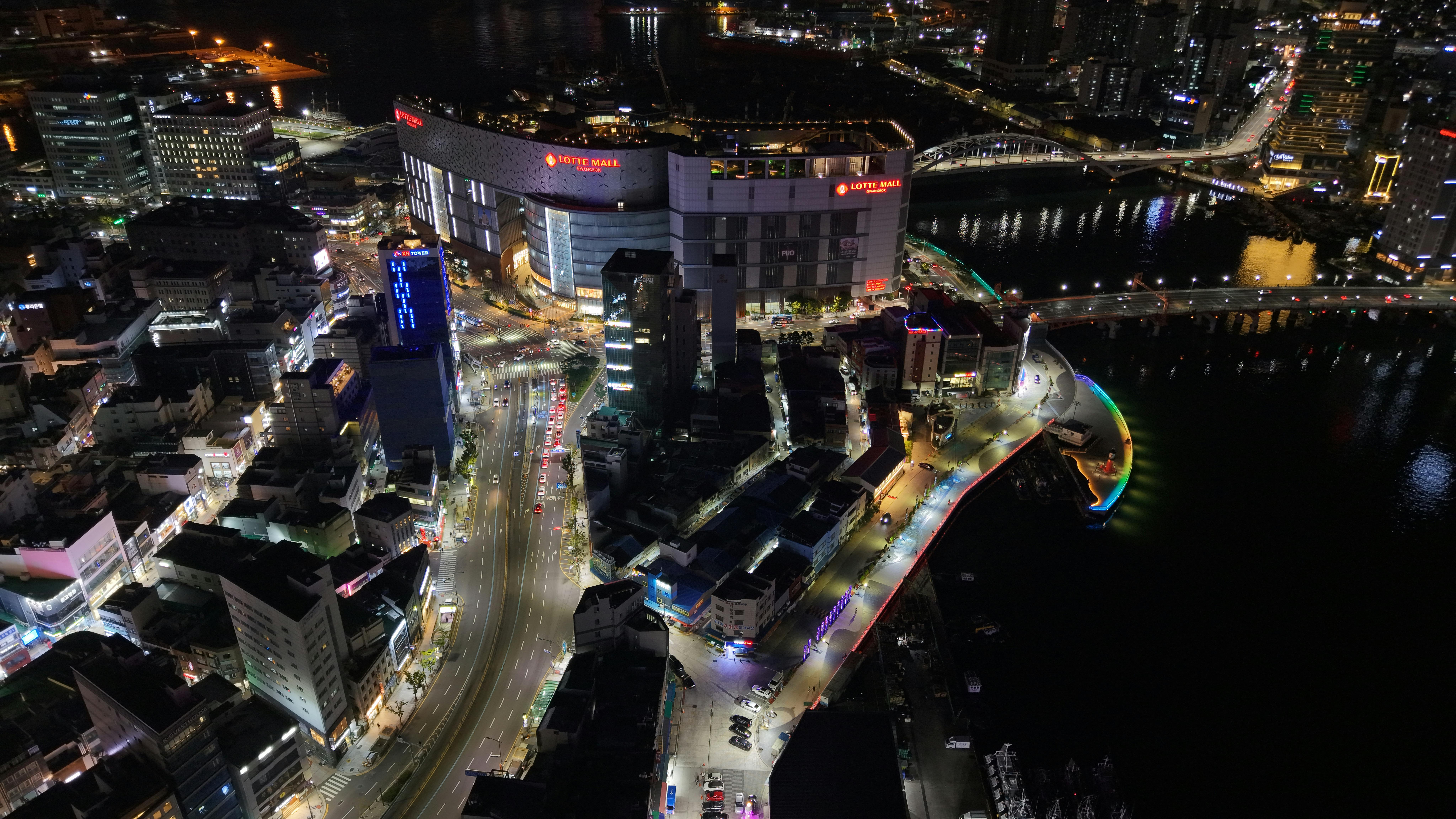 A stunning aerial shot of Busan, South Korea, featuring Lotte Mall and colorful city lights at night.