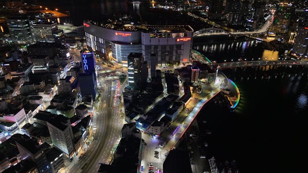 A stunning aerial shot of Busan, South Korea, featuring Lotte Mall and colorful city lights at night.