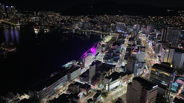 A stunning aerial shot capturing the vibrant city lights of Busan at night, showcasing urban architecture.