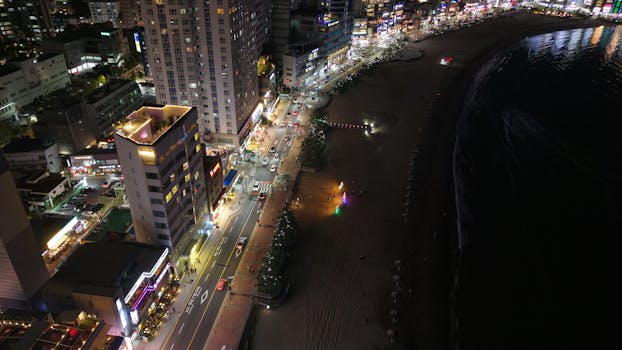 Stunning aerial night view of Haeundae Beach, Busan, showcasing vibrant city lights along the coastline.