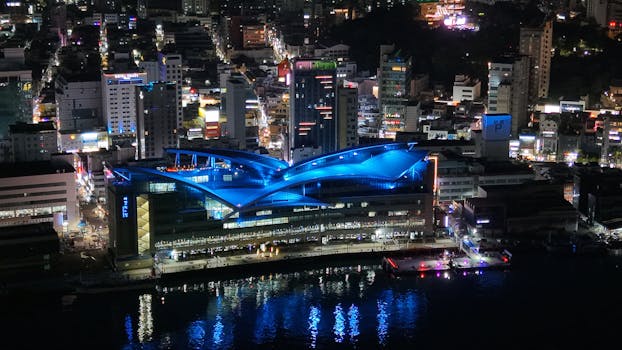 A stunning night view of Busan with its illuminated skyline and modern architecture reflecting in the water.